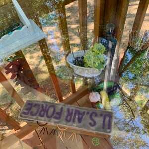 May include: A wooden table with a glass top. The table is decorated with a variety of items, including a small white planter with green plants, a bottle, and a sign that reads "U.S. AIR FORCE".