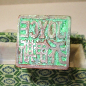 May include: A green and brown square stamp with the text "JOYCE" and Chinese characters in a decorative font.
