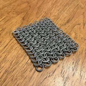 Puede incluir: Un cuadrado de malla de cadena de metal gris, hecho de anillos de metal entrelazados.