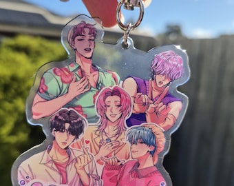 May include: A clear acrylic keychain featuring a group of anime-style characters in various poses. The keychain has a silver clasp and the words "SODA POP!!" in blue. The characters are in shades of pink, purple, and blue.