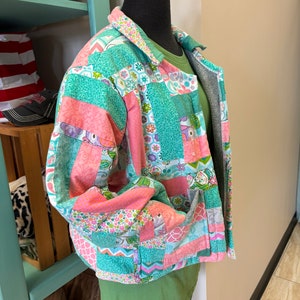 May include: A patchwork jacket in shades of pink, teal, and white, displayed on a mannequin. The jacket features a collared neckline, button closure, and pockets. The fabric is patterned with floral and geometric designs.