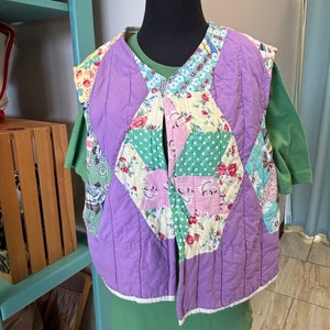 May include: A purple quilted vest with a patchwork design featuring floral and geometric patterns in shades of green, pink, and yellow.