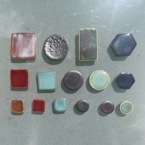 May include: A collection of ceramic tiles in various shapes and colors. The tiles include squares, circles, rectangles, and hexagons, with colors ranging from red and blue to green and brown. Some tiles have textured surfaces.