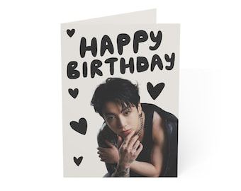 May include: A folded greeting card with the words "HAPPY BIRTHDAY" in bold black letters. The card features a photograph of a person with dark hair and tattoos, surrounded by black heart shapes.