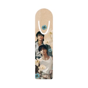 May include: A brown bookmark with a floral design featuring white flowers and blue accents. Two men are pictured on the bookmark, one with a black shirt and the other with a white tank top.