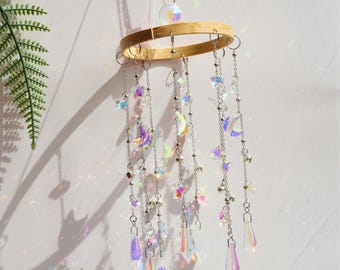 May include: A rainbow iridescent crystal mobile with stars, moons, and teardrop-shaped crystals hanging from a wooden hoop.