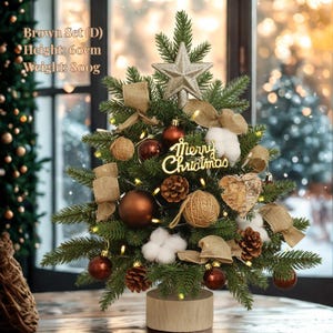 Puede incluir: Un pequeño árbol de Navidad decorado con adornos marrones, lazos de arpillera y una estrella. Tiene un letrero de "Merry Christmas". Mide unos 60 cm de alto y pesa 800g.
