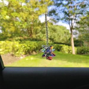 Peut inclure: Un charme de voiture en cristal avec un motif en forme de fleur. Le charme est fait de cristal clair avec des couleurs arc-en-ciel irisées. Il est suspendu à une chaîne argentée.