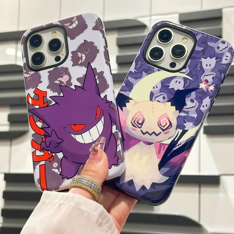 以下が含まれることがあります： ポケモンのキャラクターが描かれた携帯電話ケース2つ。最初のケースは白地に紫と赤のゲンガーのキャラクターと日本語の文字。2つ目のケースは紫地に白と黄色のゴーストのキャラクター