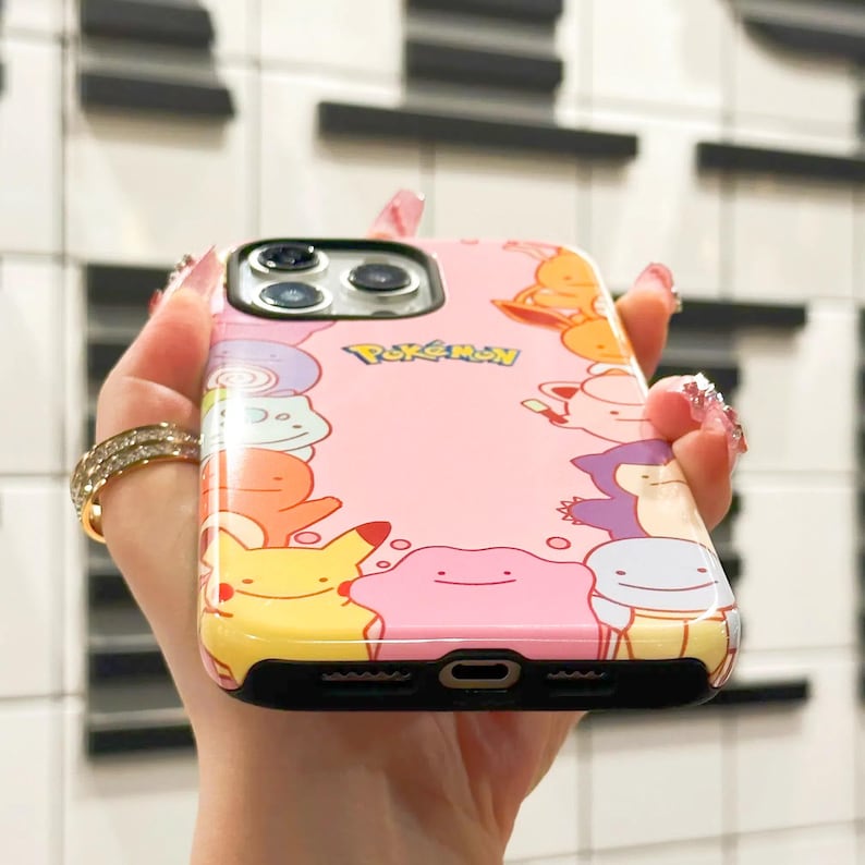 May include: A pink phone case with a Pokemon theme. The case features a variety of Pokemon characters, including Pikachu, Jigglypuff, and Squirtle. The case is made of a clear, hard plastic and has a black border.