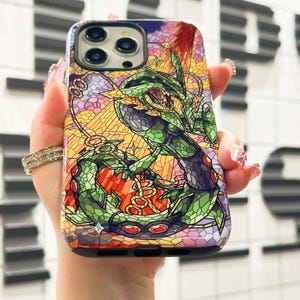 May include: A phone case with a stained glass design featuring a green and purple creature with red eyes. The case has a black border and a camera cutout.
