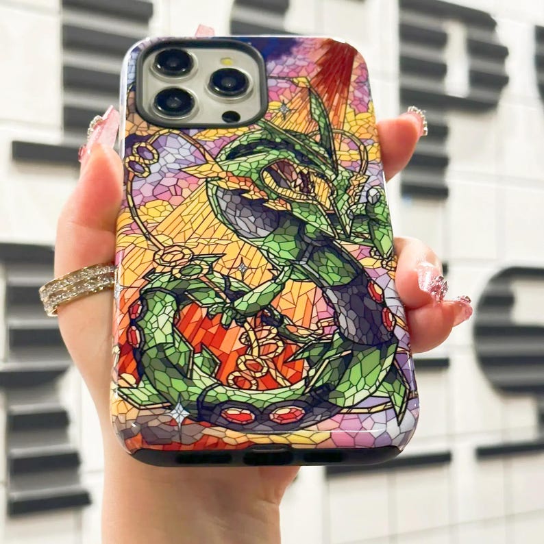 May include: A phone case with a stained glass design featuring a green and purple creature with red eyes. The case has a black border and a camera cutout.