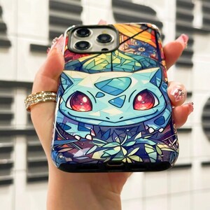 May include: A phone case with a stained glass design featuring a blue and green Pokemon character with red eyes. The background is a colorful floral pattern.