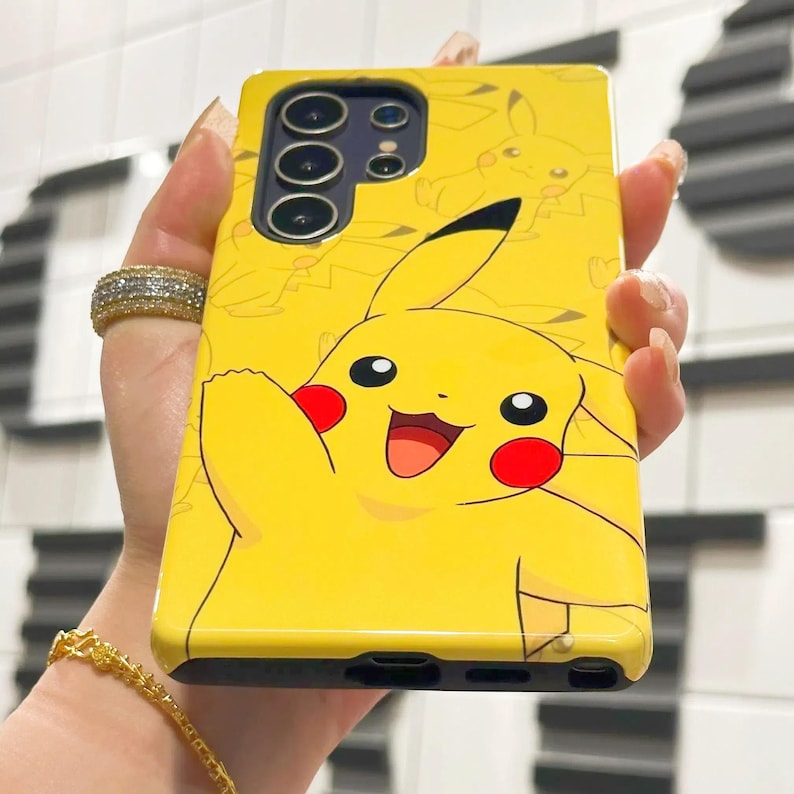 May include: A yellow phone case with a cartoon Pikachu design. The case has a black camera bump with three lenses.