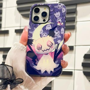 以下が含まれることがあります： 紫と白の携帯電話ケース。漫画の幽霊のキャラクターと三日月が描かれている。背景には、小さな幽霊のシルエットがぎっしり詰まっている。