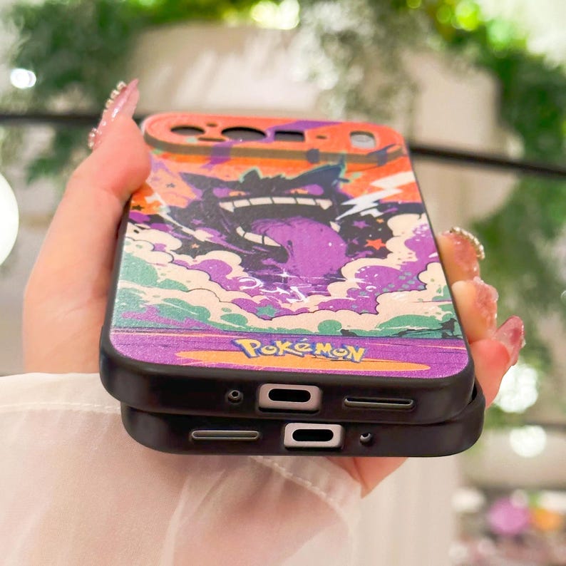 May include: A black phone case featuring a colorful illustration of a purple Gengar character with a long tongue, set against a vibrant orange and purple background. The word "Pokemon" is printed at the bottom.