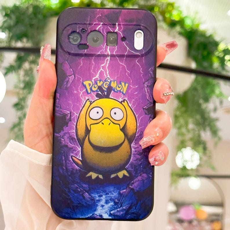 May include: A purple phone case featuring a yellow Psyduck Pok&eacute;mon character with the Pok&eacute;mon logo. The case has a lightning bolt design and a rocky landscape background.
