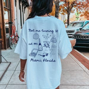 May include: White t-shirt with a navy blue design that says "Not me turning 30 est 1995 Miami, Florida" with various party-themed illustrations.
