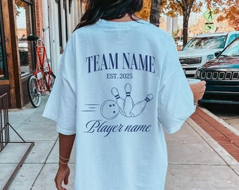 May include: White oversized t-shirt with a navy blue bowling design on the back. The design includes the text "TEAM NAME EST. 2025" and "Player name".