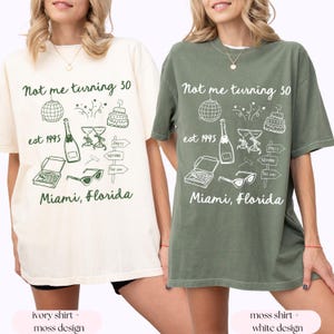 May include: Two t-shirts with a graphic design featuring the text "Not me turning 30" and various illustrations including a disco ball, champagne glasses, a pizza box, sunglasses, and a birthday cake. The shirt on the left is ivory with a green design. The shirt on the right is moss green with a white design.