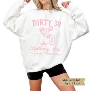 May include: White sweatshirt with the text "DIRTY 30" in pink, with a margarita and shot glass graphic. The text "EST. 1995" and "Birthday Girl" are also in pink. The text "EMILY'S 30TH - CANCUN, MEXICO" is in black.