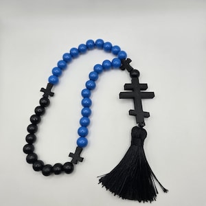 May include: A rosary featuring blue and black beads, and black crosses. A black tassel hangs from the end. The beads are spherical and smooth. The crosses have a simple design.