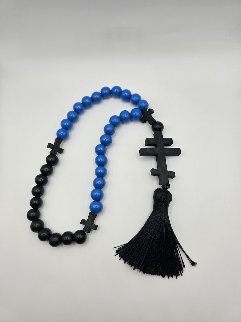 May include: A rosary featuring blue and black beads, and black crosses. A black tassel hangs from the end. The beads are spherical and smooth. The crosses have a simple design.