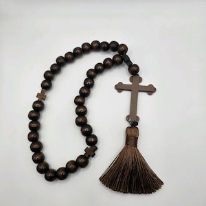 May include: A dark brown rosary with wooden beads and a cross pendant. The rosary features a tassel and small cross accents. The beads are evenly spaced, and the cross is a simple, traditional design. The rosary is likely used for prayer and meditation.