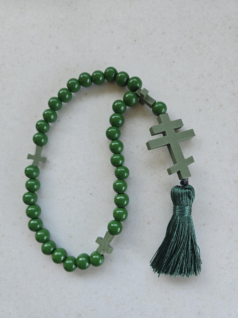May include: A dark green rosary featuring spherical beads and three cross-shaped elements. A dark green tassel is attached. The rosary is made of wood and is used for prayer and meditation.