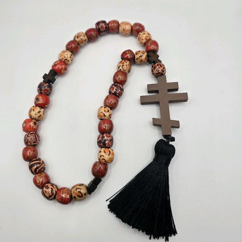 May include: A wooden rosary featuring a brown cross and a black tassel. The beads are a mix of red, brown, and tan, with patterned and solid designs. A religious item.