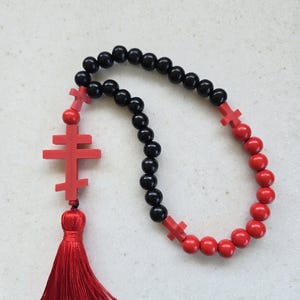 May include: A rosary with black and red beads. The rosary features red crosses and a red tassel. The beads are made of wood. The rosary is a religious item.