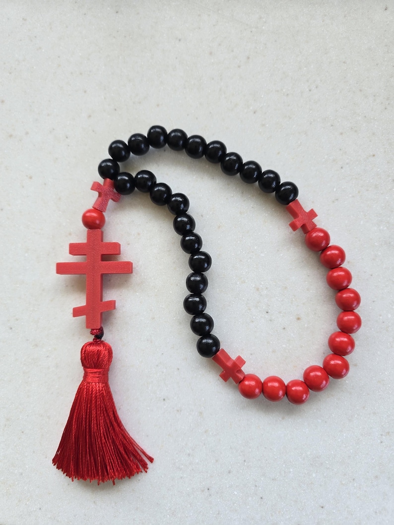 May include: A rosary with black and red beads. The rosary features red crosses and a red tassel. The beads are made of wood. The rosary is a religious item.