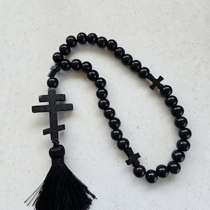 May include: Black prayer beads featuring a tassel and cross-shaped details. The beads are spherical and polished, and the tassel is made of black threads. The crosses are a simple, traditional design.