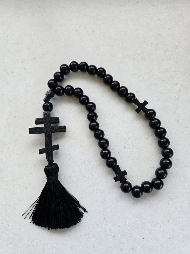 May include: Black prayer beads featuring a tassel and cross-shaped details. The beads are spherical and polished, and the tassel is made of black threads. The crosses are a simple, traditional design.