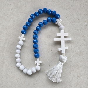 May include: A rosary featuring blue and white beads. The beads are spherical and linked together. White crosses are interspersed between the beads. A white tassel is suspended from the rosary's base.