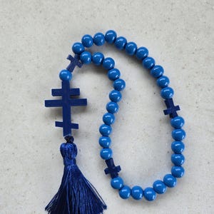 May include: A blue rosary featuring round beads and cross-shaped details. The rosary has a tassel and is made from wood or a similar material. The beads are a bright shade of blue.