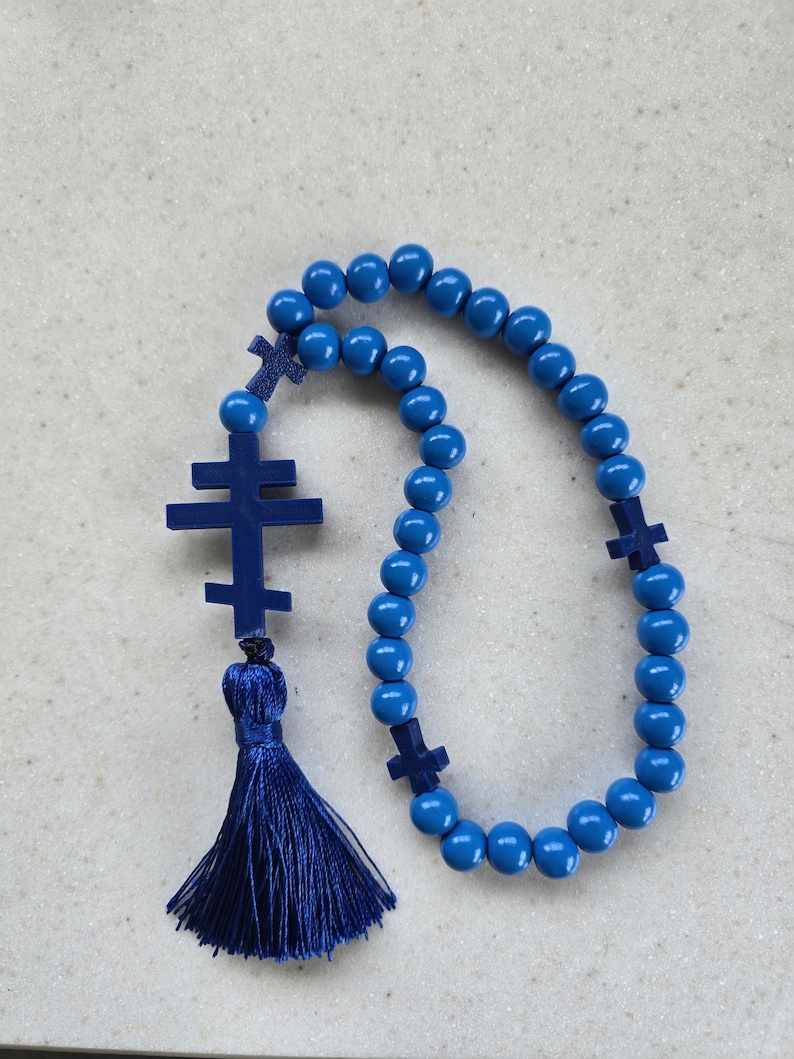 May include: A blue rosary featuring round beads and cross-shaped details. The rosary has a tassel and is made from wood or a similar material. The beads are a bright shade of blue.