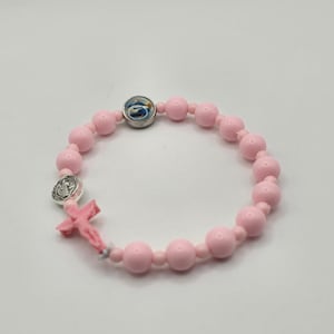 May include: A pink rosary bracelet with round beads. The bracelet features a small pink cross, a silver medal, and a circular charm with a blue and white image. The beads are evenly spaced.