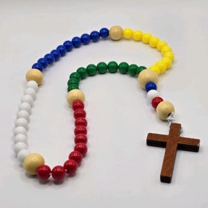 May include: A colorful rosary with wooden beads in white, red, green, yellow, and blue. The rosary features a wooden cross at the end and larger, neutral-colored beads separating the colored beads. Religious item.