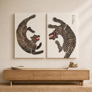 May include: Two rectangular wall art canvases featuring stylized black and white striped tigers in dynamic poses. Each tiger has a visible red mouth with sharp teeth. The right canvas includes vertical black Asian characters in the upper corner.
