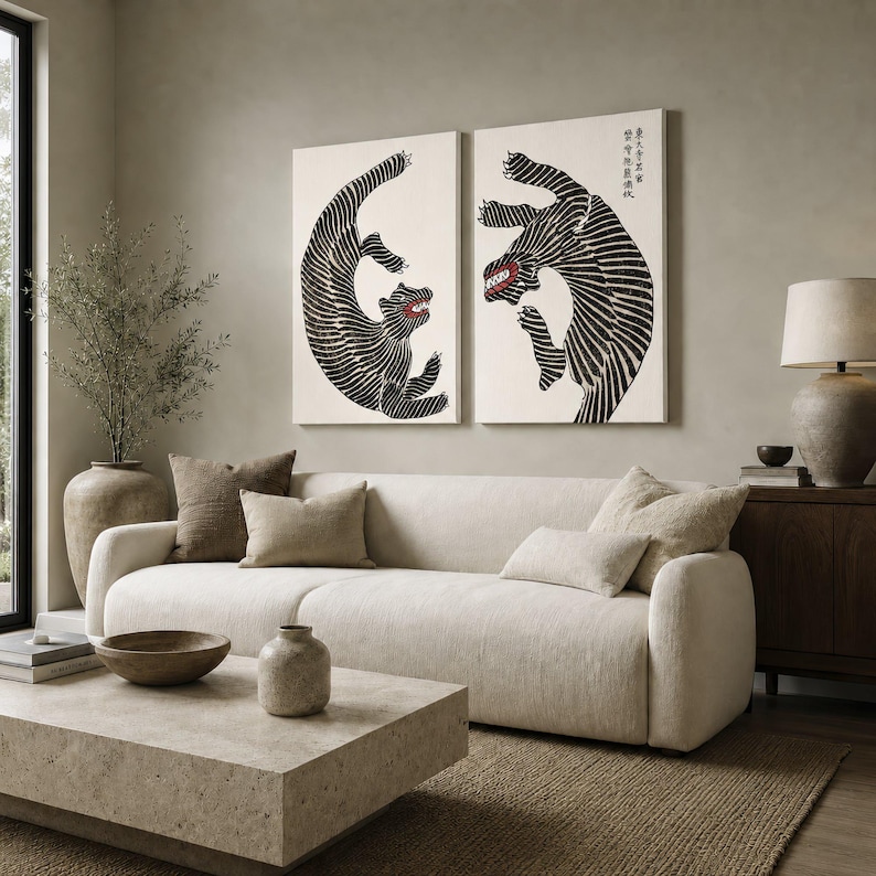 May include: Two rectangular wall art prints featuring black and white striped tigers in dynamic poses against a cream background. The tiger on the right includes vertical black Japanese text in the upper right corner. Both tigers have red mouths.