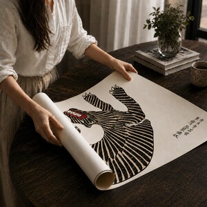 May include: A rectangular paper print featuring a black and white graphic illustration of a stylized creature with striped patterns and a red mouth. The print includes vertical Japanese text on the right side and is partially rolled at the bottom edge.