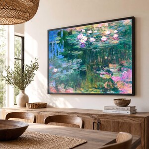 May include: A rectangular wall art print featuring an impressionist painting of a water lily pond with vibrant shades of green, blue, and pink. The artwork is enclosed in a thin black frame and displayed on a light-colored wall above a wooden sideboard.