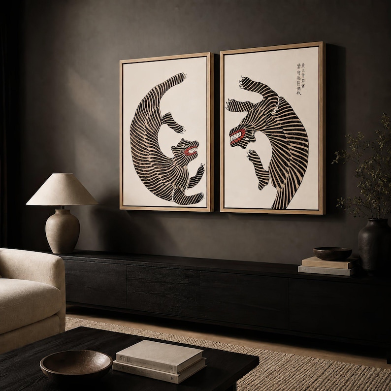 May include: Two rectangular framed wall art pieces featuring stylized black and white tiger illustrations on a cream background. Each tiger is depicted in a dynamic, curved pose with visible red accents in the mouth area and black calligraphy text.