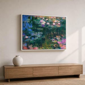 May include: A rectangular framed wall art print featuring an impressionist painting of a pond with water lilies. The artwork displays deep green, blue, and purple tones with highlights of pink and white flowers floating on the water surface.