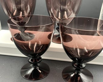 May include: Four vintage wine glasses with a dark purple hue. The glasses have a rounded bowl shape, a short stem with a bulbous detail, and a circular base. The glasses are made of glass and are arranged on a white surface.
