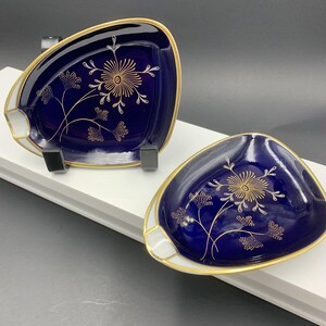 May include: Two cobalt blue ceramic ashtrays with gold trim and a floral design. The ashtrays are triangular in shape with a white rim.
