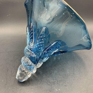 May include: A blue glass vase with a textured, bubbled surface and a clear glass base. The vase has a unique, organic shape with a wide opening and a narrow base.