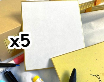 May include: A set of five blank white cards with gold trim, packaged in a brown box. The cards are stacked on top of each other and have a subtle texture. The box has a label with the number "x5" on it.