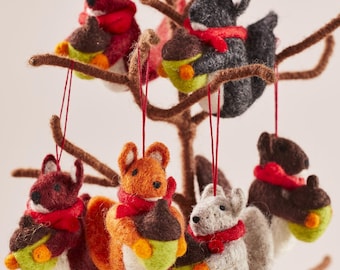 May include: A collection of felt squirrel ornaments in various colors, each holding a felt acorn. The squirrels wear red scarves and hang from brown branches. These festive decorations are perfect for a holiday tree.